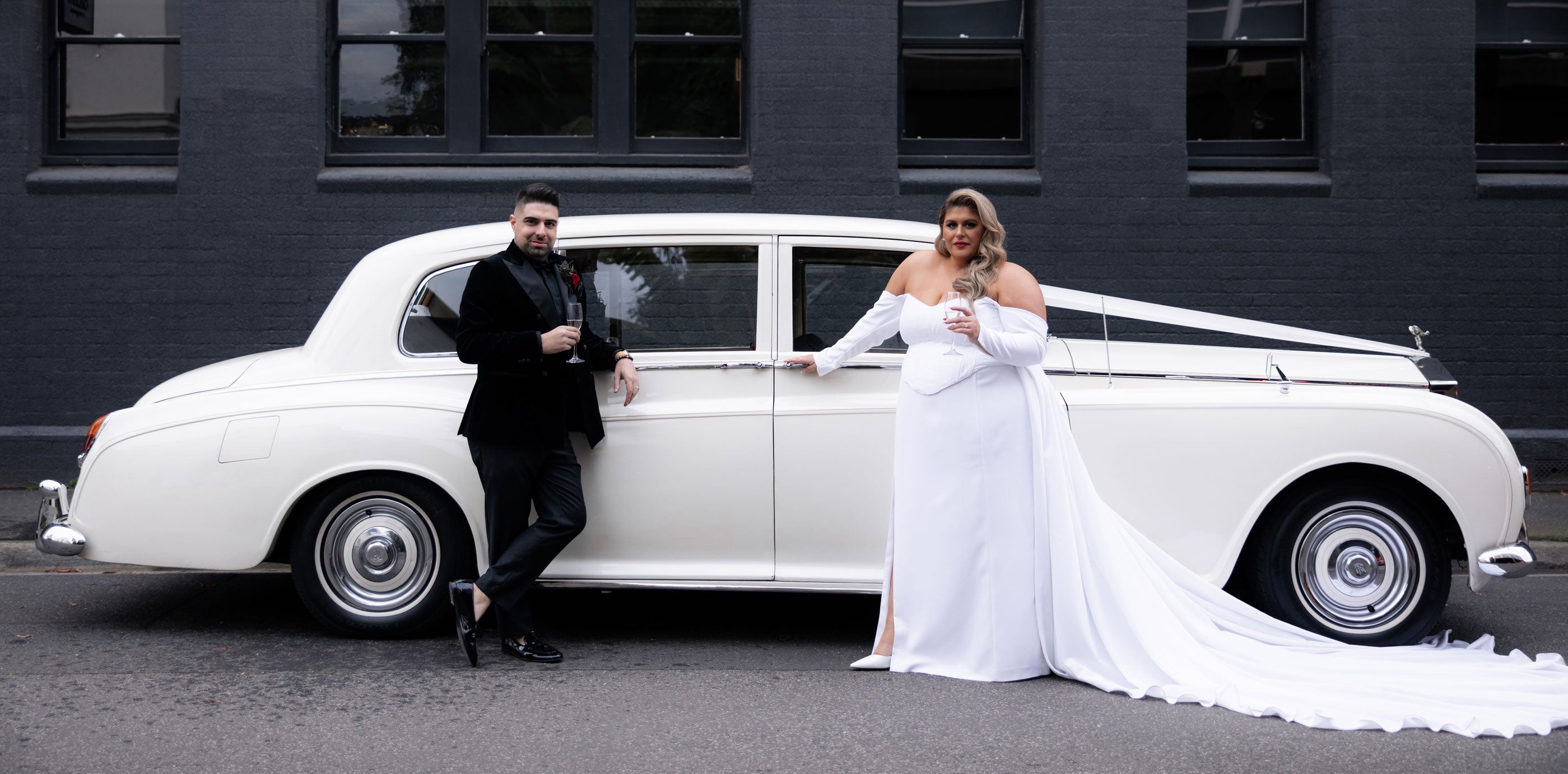 Plus size wedding dress in white. custom made Hope and Harvest Wedding gown. Melbourne Wedding Designer. Bride stands in front of classic Jag in wearing white. Groom wears black suit