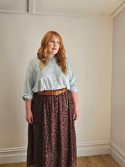 Woman wearing a light blue shirt and leopard print skirt against a plain wall.