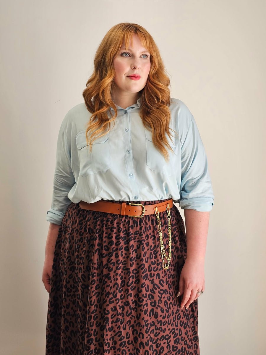 Woman wearing a light blue shirt and leopard print skirt against a plain background