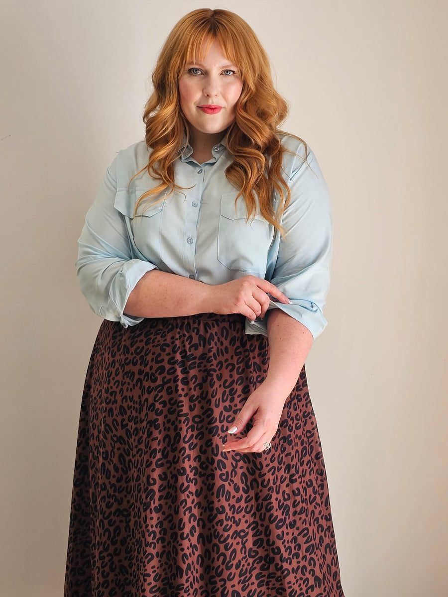 Woman wearing a light blue shirt and leopard print skirt against a plain background