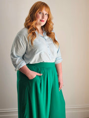 Woman wearing a light blue shirt and green pants against a plain background