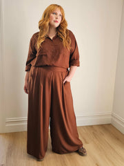 Woman wearing a pair of chocolate coloured wide leg pants and shirt by Hope and Harvest.