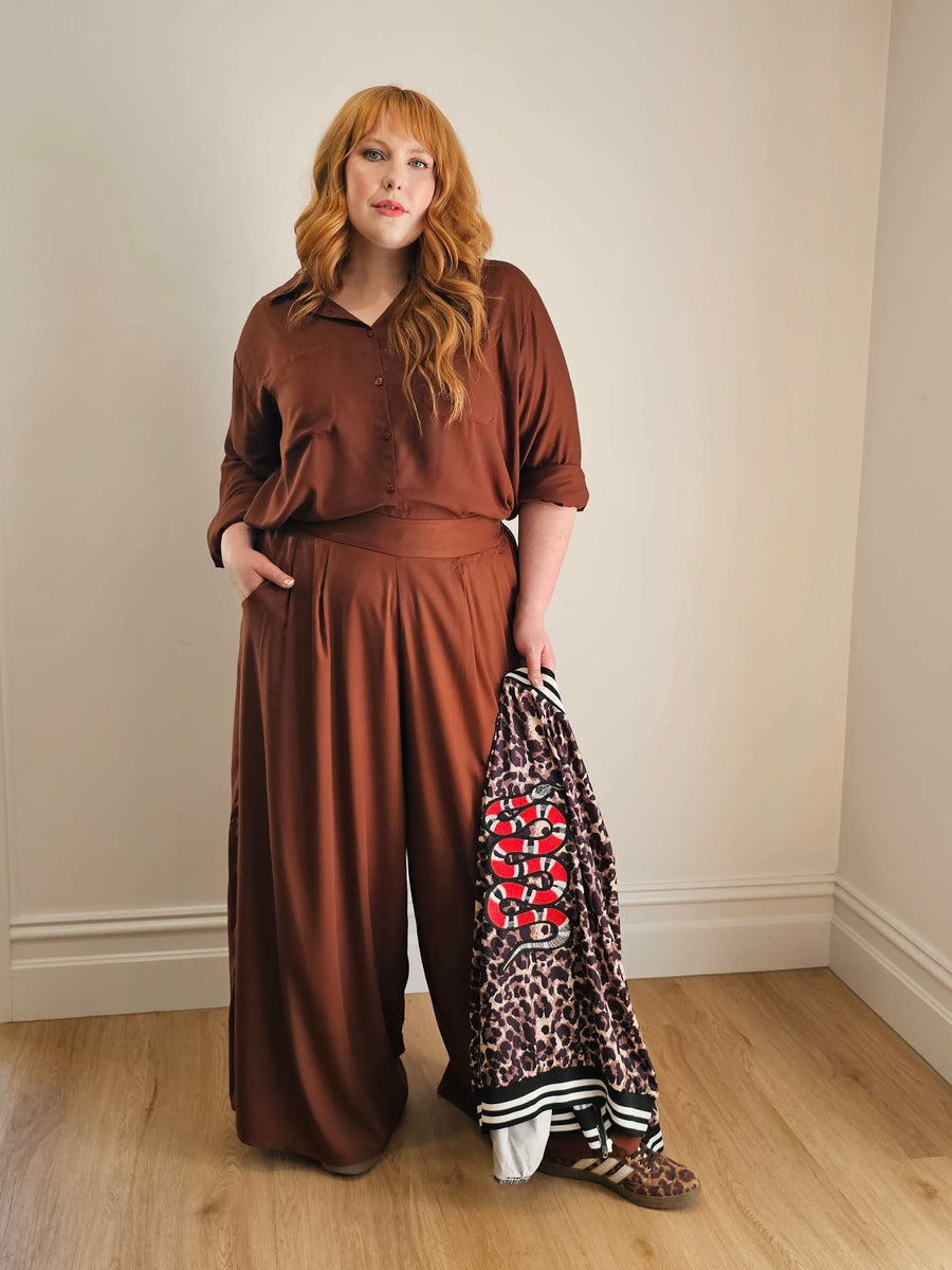 Woman in brown outfit holding a leopard print jacket with snake patch